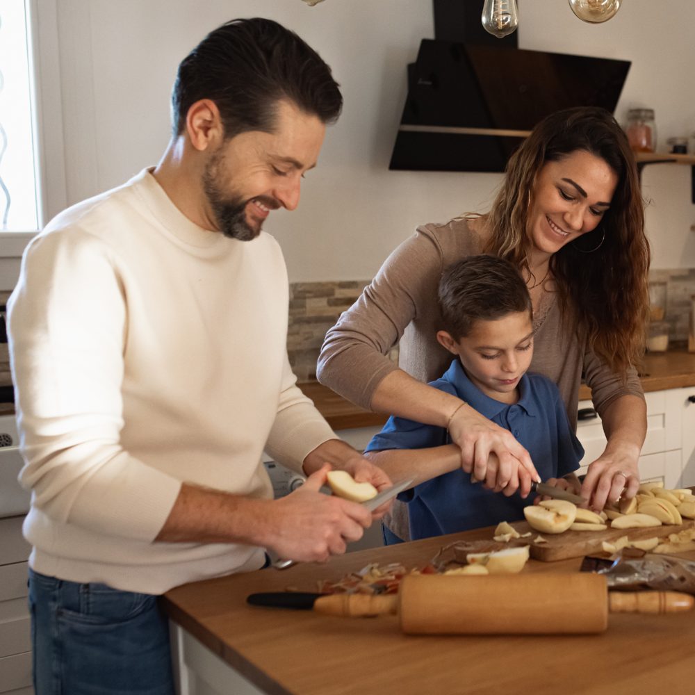 A family cooking together in a bright kitchen, slicing apples