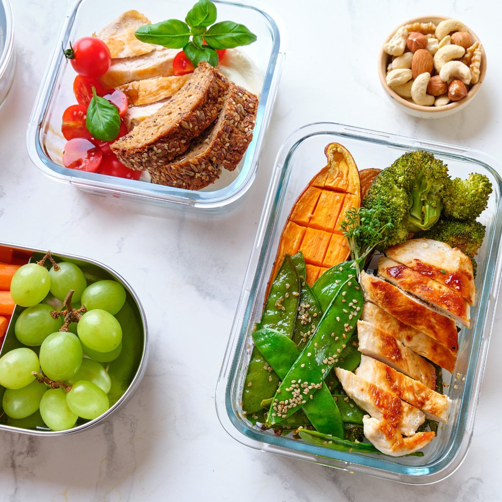 Glass food storage containers filled with chicken, vegetables, bread, and fruit