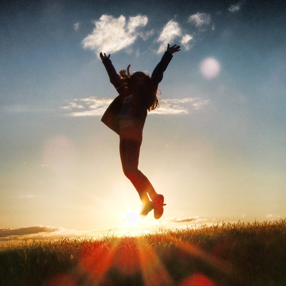 Silhouette of a person jumping with arms raised at sunrise