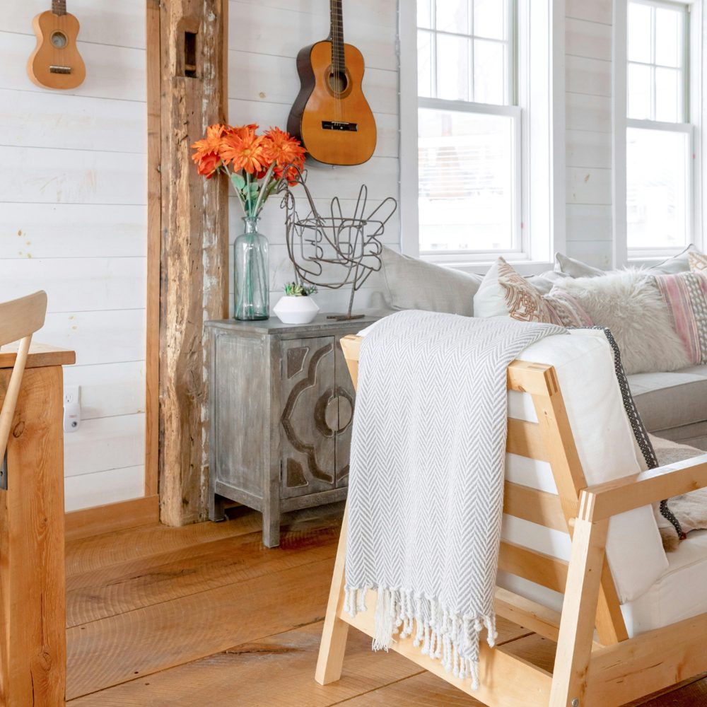 A gray herringbone throw draped over a wooden chair beside orange flowers and guitars hanging on a white plank wall